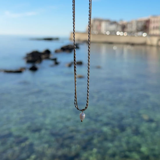 Video einer goldenen Kette mit Perlenanhänger mit Meer im Hintergrund