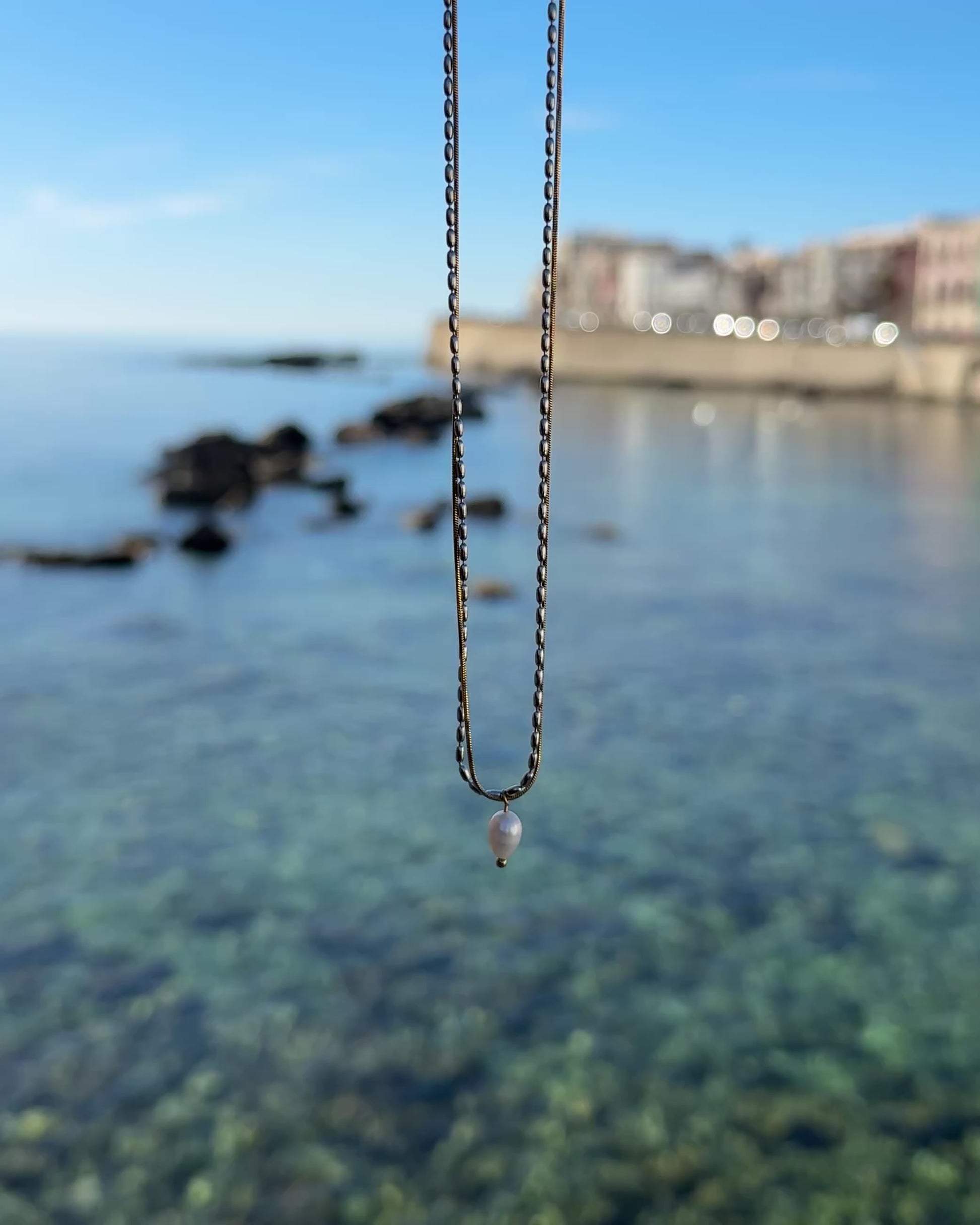 Video einer goldenen Kette mit Perlenanhänger mit Meer im Hintergrund