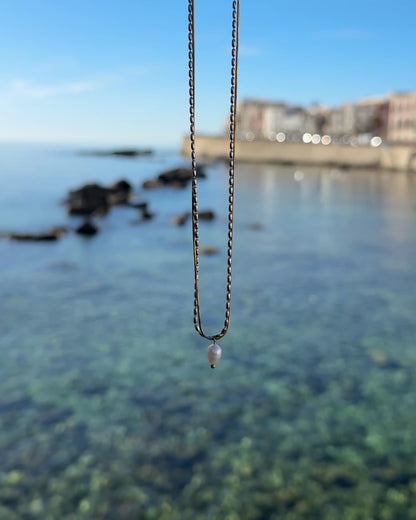 Video einer goldenen Kette mit Perlenanhänger mit Meer im Hintergrund
